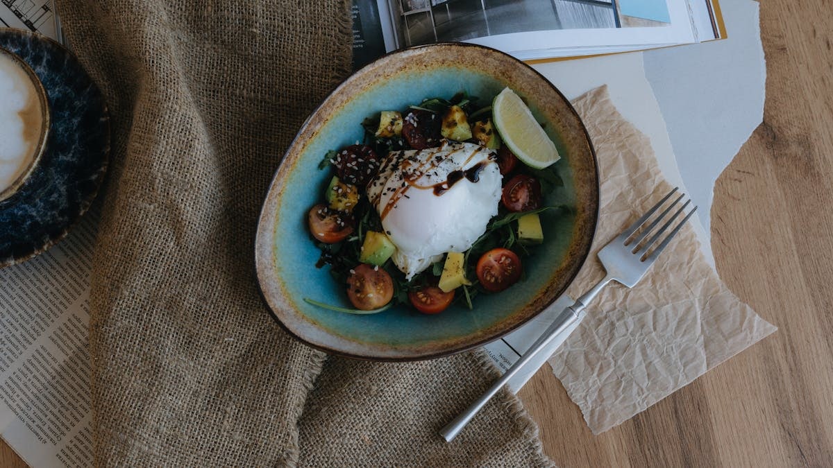 Top view of a delicious breakfast bowl with poached egg, avocado, cherry tomatoes, and lime.